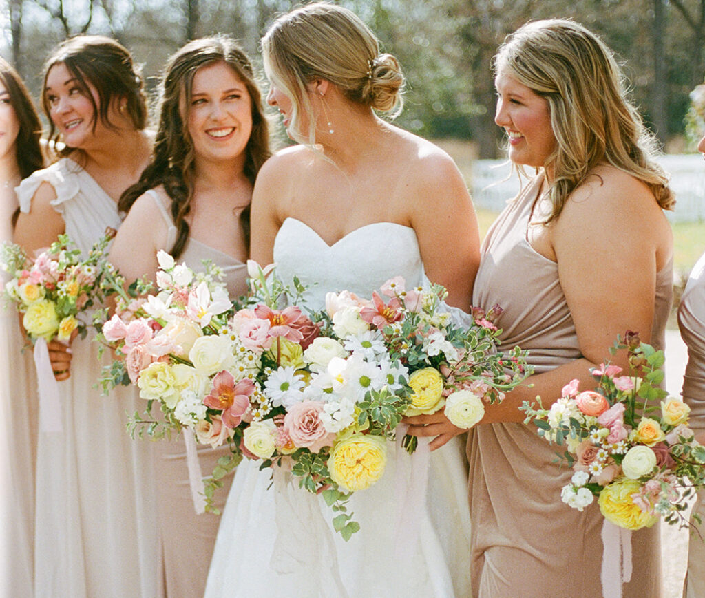 A beautiful bride with her bridesmaids, all holding stunning garden bouquets with pastel spring blooms.