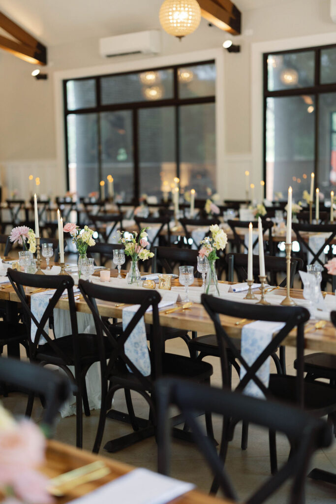Elegant wedding reception setup with taper candles, bud vases, and cross-back chairs, showing how venue managers handle layout while coordinators manage design execution and flow.

