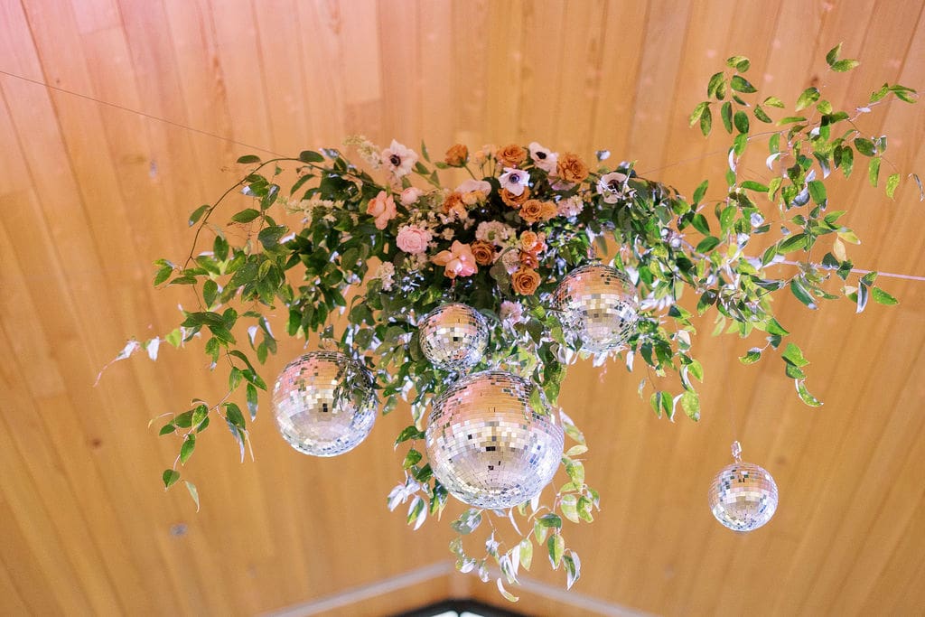 Hanging floral installation with disco balls and greenery—an eye-catching statement moment that’s perfect for wedding design ideas on a budget in Texas.
