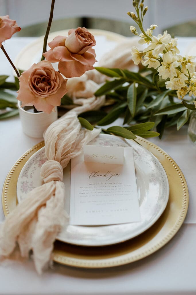Close-up of wedding menu with blush roses, greenery, and textured napkin