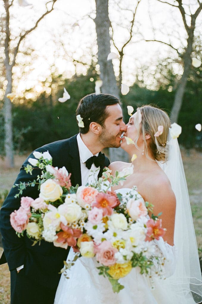 Bride and groom kissing under falling petals planned by Austin wedding planner Moments by Maddie during a fall wedding in Texas